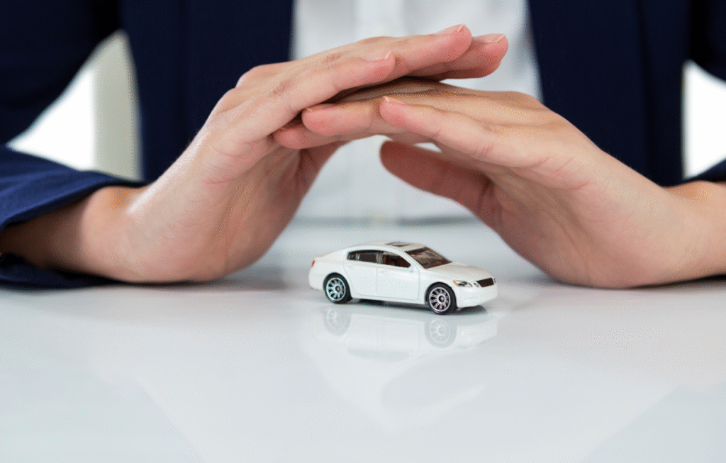 Una persona vestida con un traje oscuro sostiene las manos de forma protectora sobre un pequeño coche de juguete blanco colocado sobre una superficie blanca brillante.